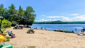 A beach with picnic tables, kayaks, and a clear view of the lake.