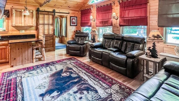 A cozy cabin interior with a fireplace, leather sofas, and a large rug.