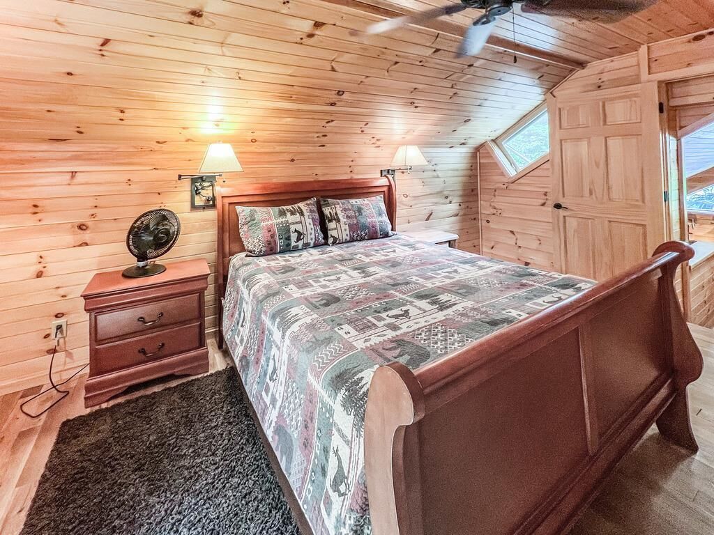 Een slaapkamer met houten lambrisering, een bed, twee bedlampen, een nachtkastje en een plafondventilator.