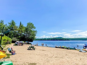 Una playa con una mesa de picnic, sombrillas y barcos.