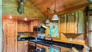 A rustic kitchen with wooden cabinets, a stove, and a hanging deer head.