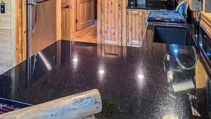 A wooden cabin interior with a kitchen area featuring a stainless steel refrigerator, a black countertop, and a deer head light fixture.