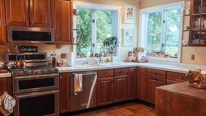 A modern kitchen with wooden cabinets, stainless steel appliances, and a large window providing natural light. - The ultimate cottagecore experience in a serene country setting overlooking USA's #1 State Park (Perry)