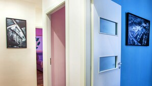 Un couloir doté d’un plancher en bois, d’une porte blanche ornée de trois fenêtres et d’un mur bleu sur lequel est accroché un tableau encadré.
