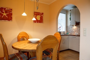 A dining area with a round wooden table, four wooden chairs with colorful cushions, and two pendant lights.
