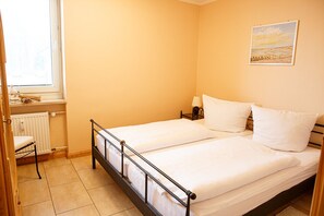 A bedroom with two single beds, a window, a radiator, and a painting on the wall.