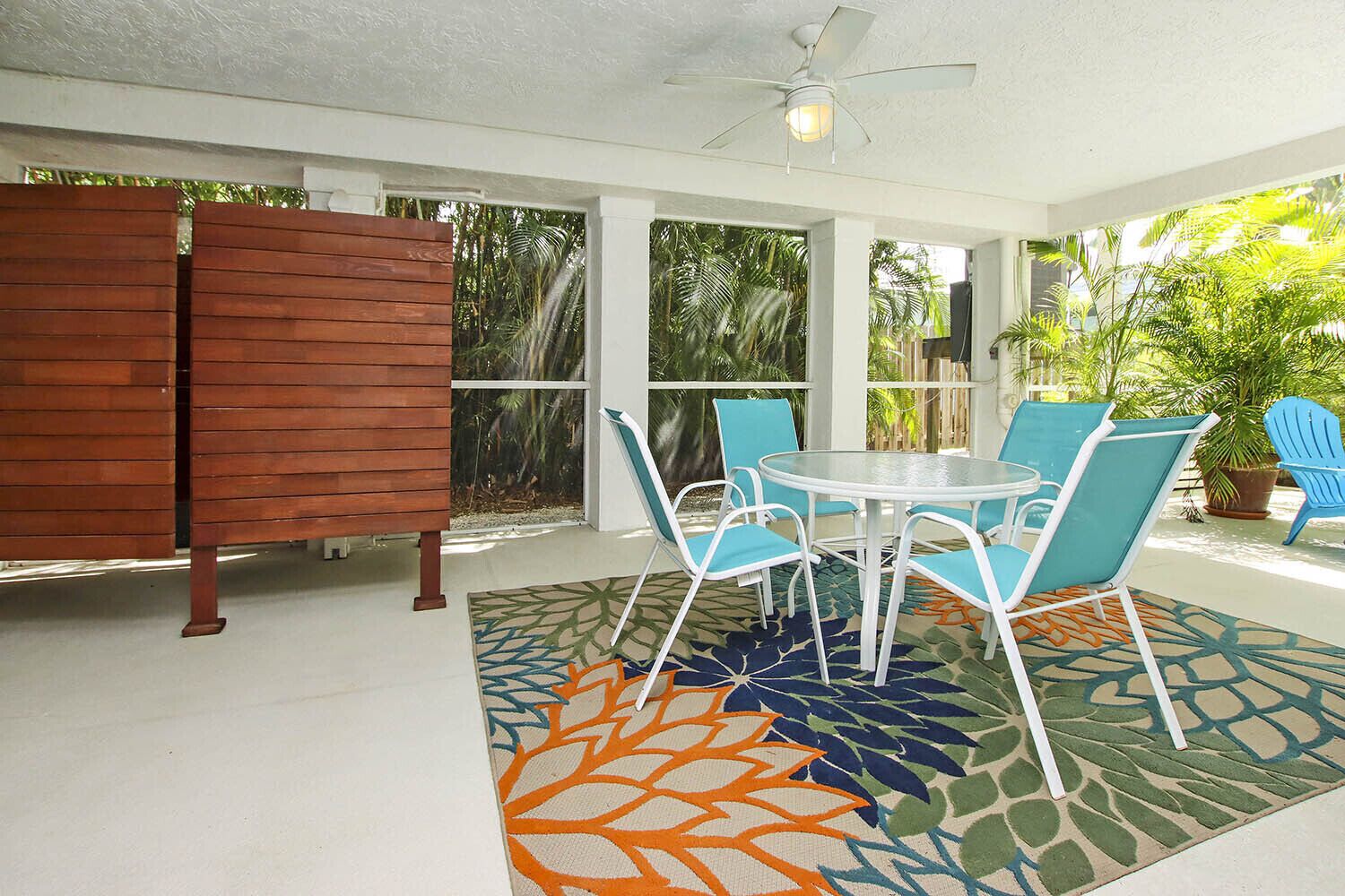 A covered patio with a round table and blue chairs, surrounded by a patterned rug and wooden partitions.
