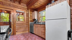 Ein Holzblockhaus-Interieur mit Küchenzeile, inklusive Schränken, einem Kühlschrank und einer Kaffeemaschine.