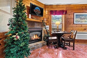 A cozy room with a fireplace, a Christmas tree, a television, and a dining area.