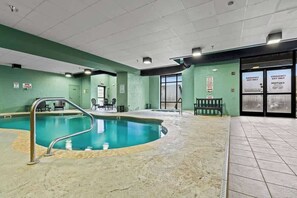 Piscina interior con trampolín, zona de spa y señales de salida de emergencia.