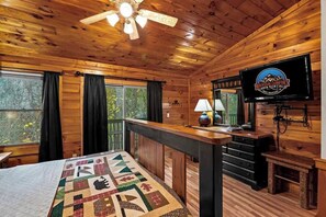 Interior de una cabaña con una cama, un escritorio, un televisor y una ventana con cortinas.