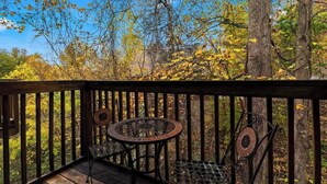 Eine Holzterrasse mit Metallstühlen und einem Tisch, mit Blick auf ein bewaldetes Gebiet im Herbstlaub.