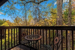 A wooden deck with metal chairs and a table, overlooking a forested area with autumn foliage. - Cozy Mountain Retreat w Pools &Free Attraction Tix (Pigeon Forge)