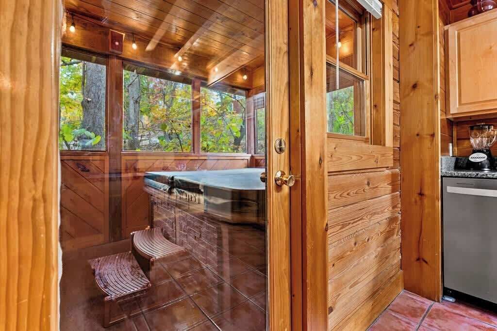 A wooden interior with a sauna, a window with a view of trees, and a kitchen area.