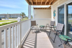 A balcony with white railings, a covered area, and a view of a building in the background. - OW 9101 - Days Drift By: A cozy oceanview condo in Oak Island, perfect for families. (Oak Island)