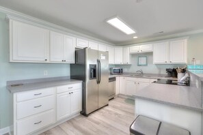 A modern kitchen with white cabinetry, a stainless steel refrigerator, a microwave, and a dishwasher. - OW 9101 - Days Drift By: A cozy oceanview condo in Oak Island, perfect for families. (Oak Island)