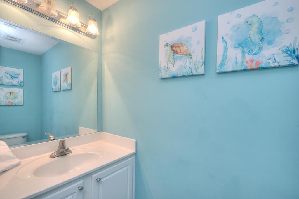 A bathroom with a light blue wall, a white sink, and a mirror. There are three framed paintings on the wall depicting underwater scenes.