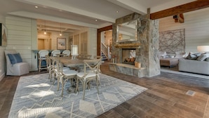 Un vaste salon agrémenté d’une cheminée en pierre, un coin repas avec une table et des chaises en bois, et un espace salon confortable avec un canapé et des fauteuils.