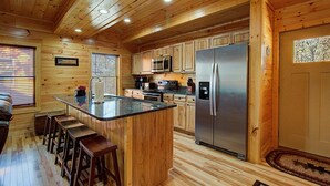 A wooden cabin-style kitchen with a central island, bar stools, a refrigerator, microwave, and a sink. - Close To Pigeon Forge Attractions/ Seasonal Outdoor Pool/ Perfect For Families! (Pigeon Forge)