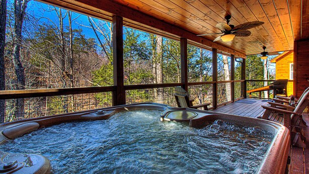 A hot tub area with wooden deck and large windows overlooking a forest. - Close To Pigeon Forge Attractions/ Seasonal Outdoor Pool/ Perfect For Families! (Pigeon Forge)