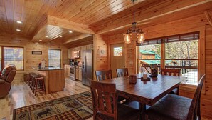 A spacious wooden cabin with a large dining table, kitchen area, and a cozy seating area. - Close To Pigeon Forge Attractions/ Seasonal Outdoor Pool/ Perfect For Families! (Pigeon Forge)