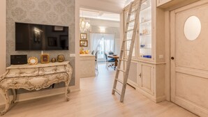 Una habitación con un televisor sobre un mueble blanco ornamentado, una escalera y una puerta con un espejo redondo.