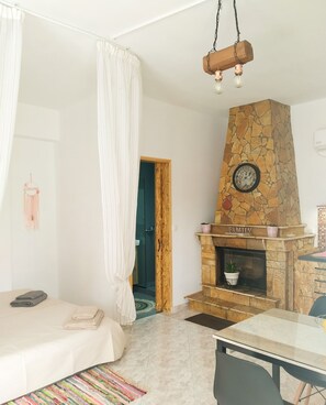 A bedroom with a bed, a bedside table, a stone fireplace, a clock, and a door leading to another room.