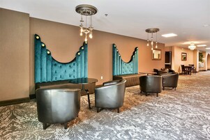 Un hall de hotel con alfombra estampada, zona de estar con sofás y sillones, y una pared decorativa con un diseño único.