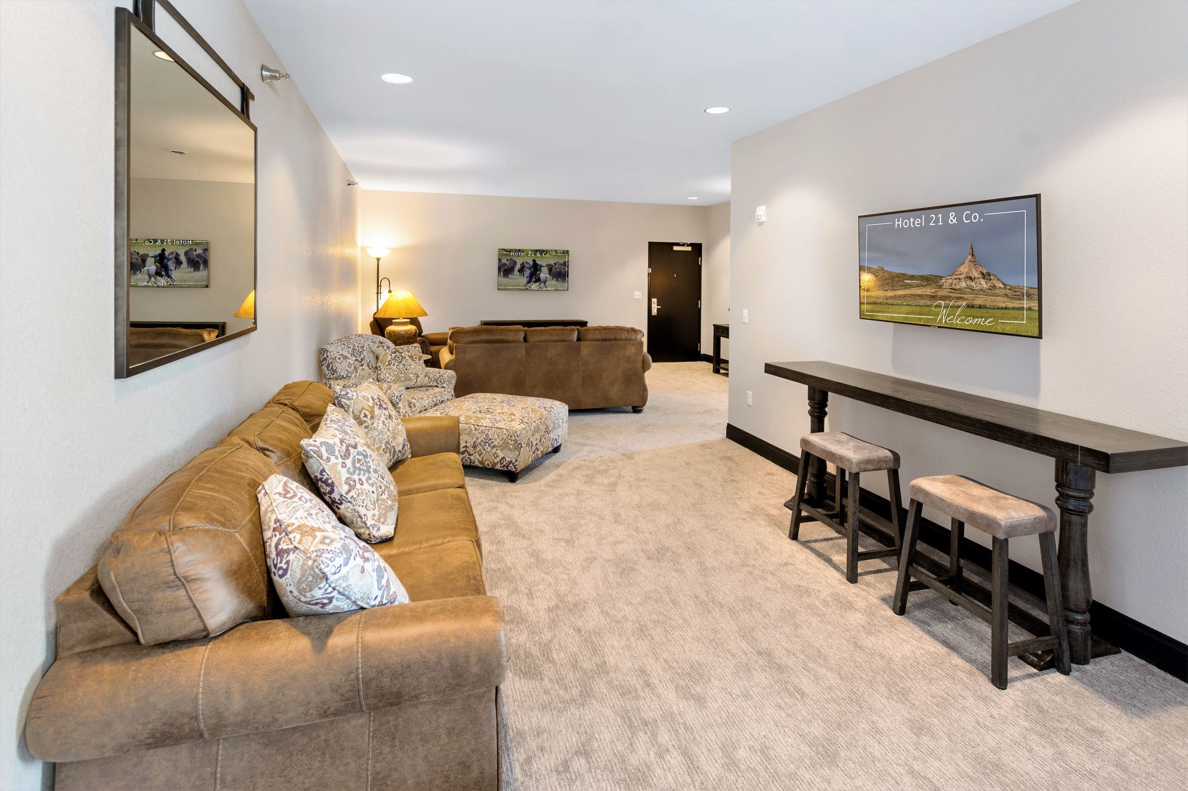 A spacious living area with a brown leather sofa, patterned cushions, a wooden coffee table, and a bar with stools.