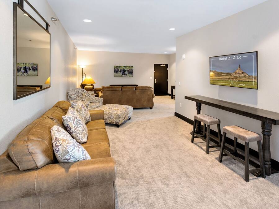 A spacious living area with a brown leather sofa, patterned cushions, a wooden coffee table, and a bar with stools.