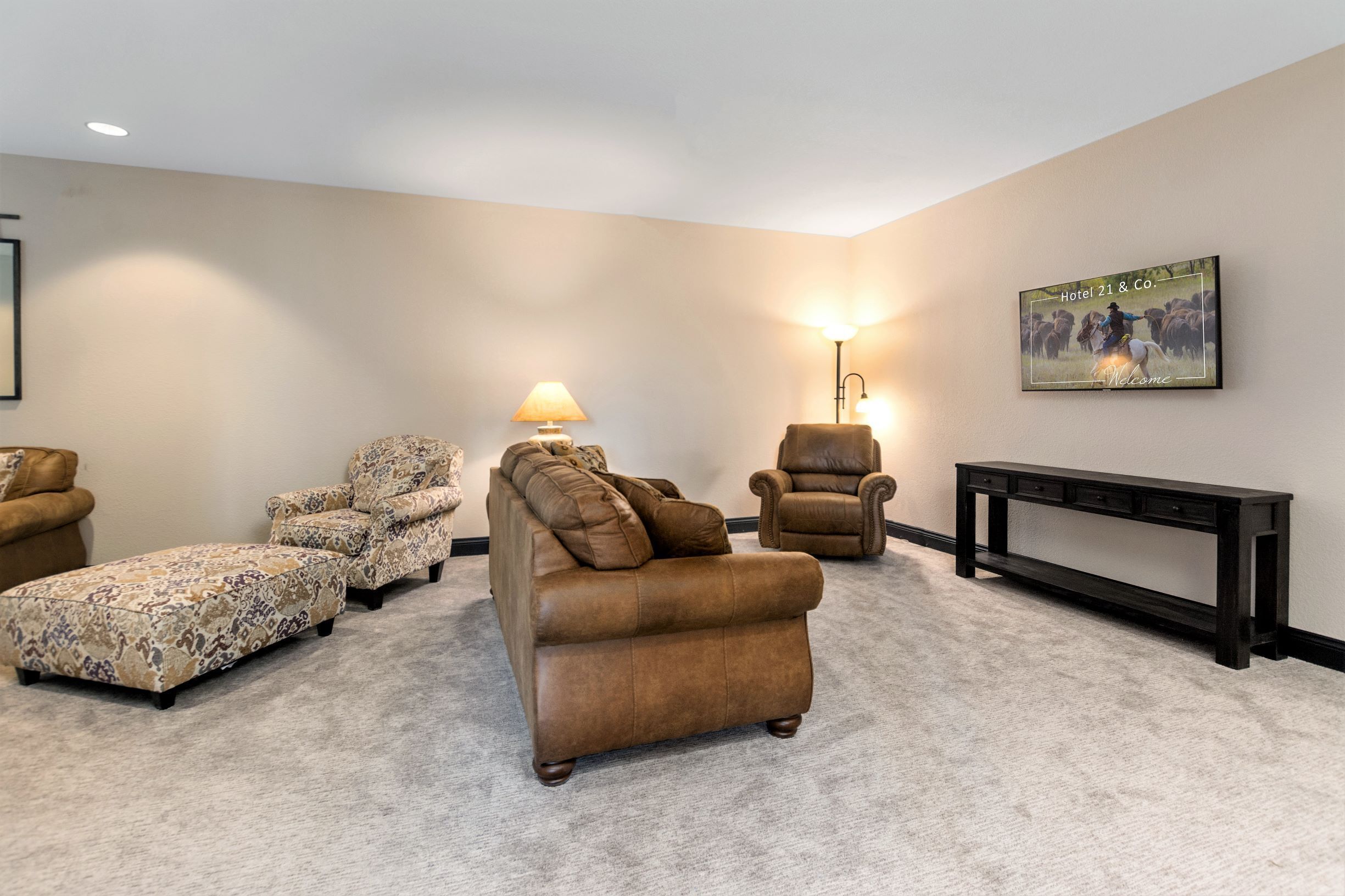 A living room with a brown sofa, patterned armchairs, a lamp, and a fireplace.