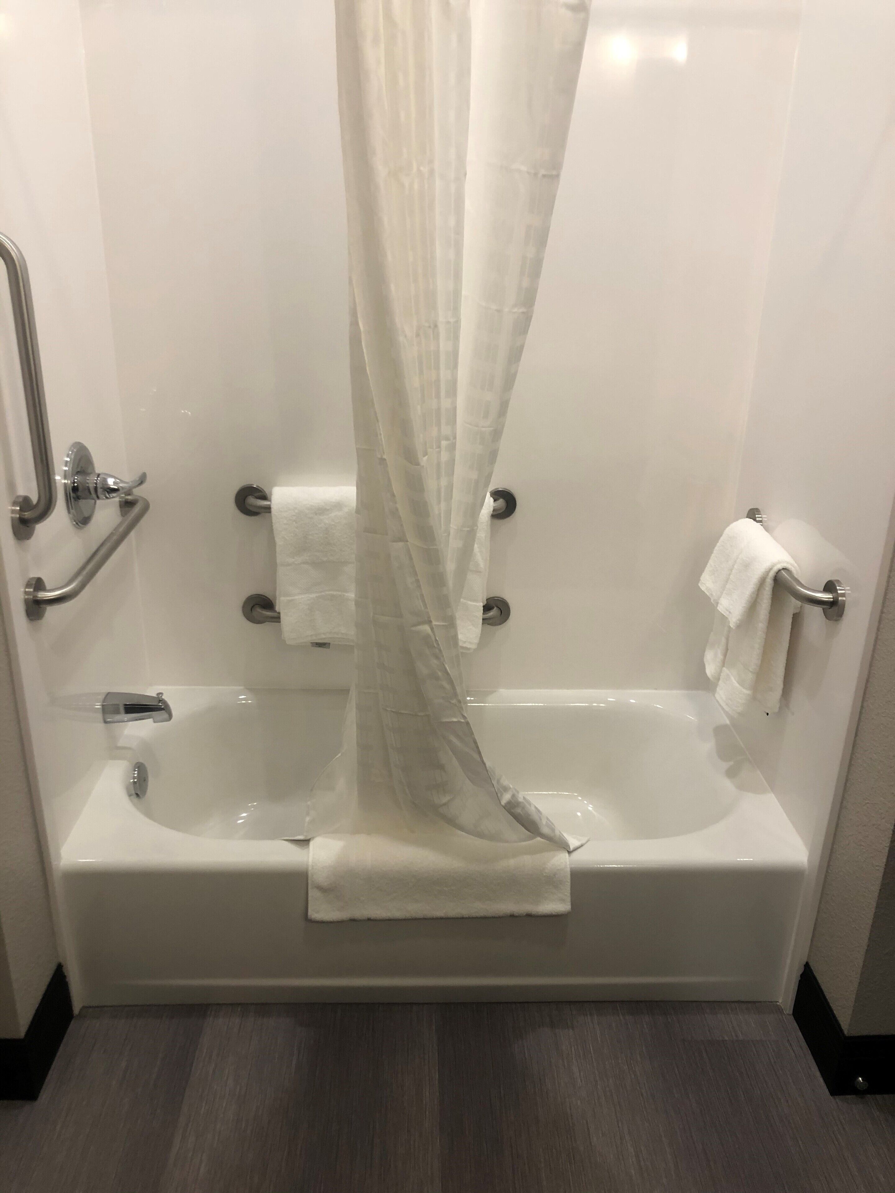 A modern bathroom with a bathtub, a shower curtain, grab bars, and a towel rack.