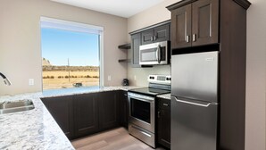 A modern kitchen with dark cabinetry, stainless steel appliances, and a large window offering a view of a desert landscape. - Hotel 21 & Co. (Gering)
