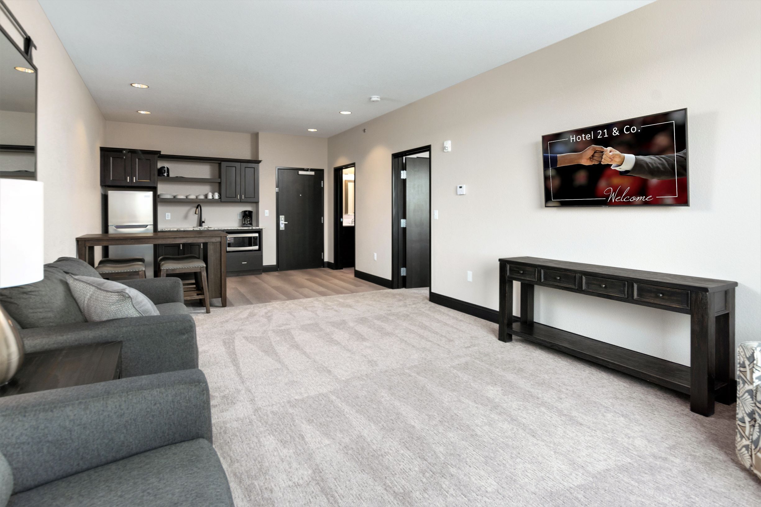 A modern living room with a grey sofa, a wooden coffee table, and a kitchen in the background.