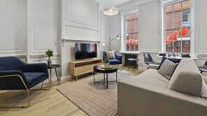 A modern living room with a TV, sofa, chairs, and a coffee table. - Gerrard Place by Aeria Apartments (London)