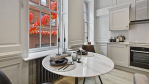 A modern kitchen with white cabinetry, a built-in oven, and a dining area with a round table set for two. - Gerrard Place by Aeria Apartments (London)