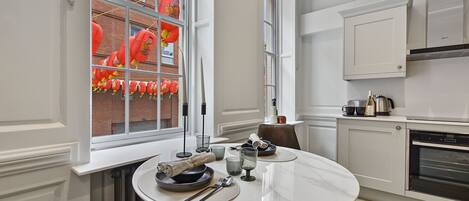 A modern kitchen with white cabinetry, a built-in oven, and a dining area with a round table set for two.