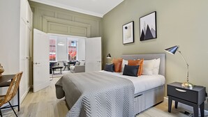 A bedroom with a bed, bedside table, lamp, and a view of a dining area. - Gerrard Place by Aeria Apartments (London)