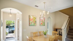 A dining area with a wooden table and chairs, a chandelier, and two floral paintings on the wall. - 3BR Family Resort Townhouse - Lazy River & Water Slide - Disney 15 Min (Davenport)