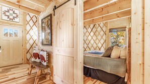 A wooden cabin interior with a bed, a bench, and a door. - Cozy Blue-Beary great f/ couples or small family, Huge Deck w/Privte Hot Tub (Pigeon Forge)
