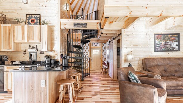 A wooden interior with a kitchen, dining area, and a staircase leading to a loft. - Cozy Blue-Beary great f/ couples or small family, Huge Deck w/Privte Hot Tub (Pigeon Forge)