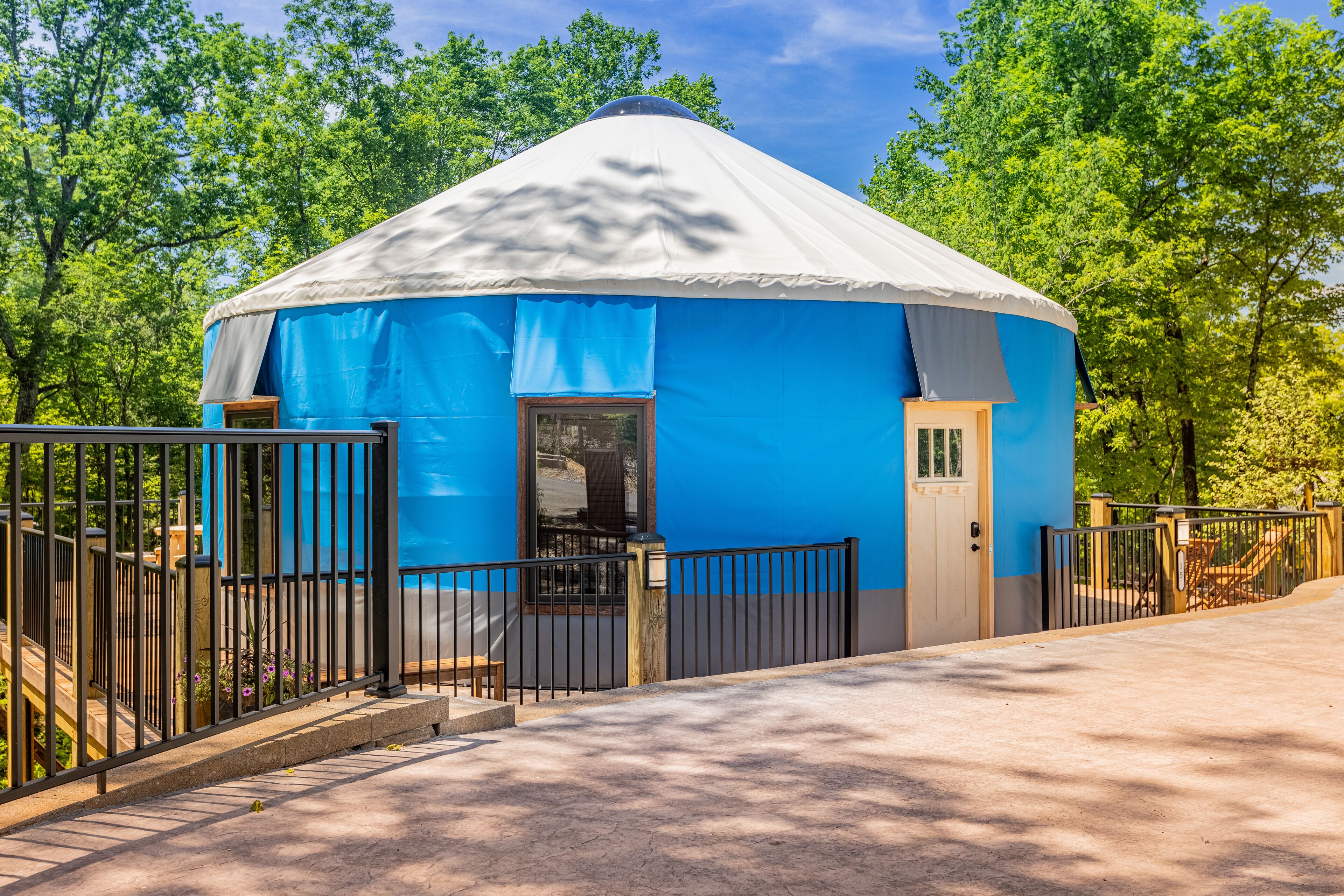 A blue and white yurt with a door and window, surrounded by a fence and trees.