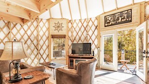 A cozy interior with a sofa, table, and TV, wooden walls, and a balcony with a view of trees. - Cozy Blue-Beary great f/ couples or small family, Huge Deck w/Privte Hot Tub (Pigeon Forge)