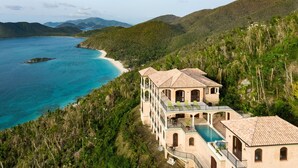 Ein großes, mehrstöckiges Gebäude mit Pool, umgeben von üppiger Vegetation und mit Blick auf das türkisfarbene Meer.