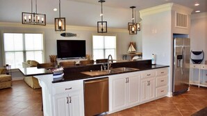 Una cocina amplia con una isla grande, armarios blancos, electrodomésticos de acero inoxidable e iluminación colgante.