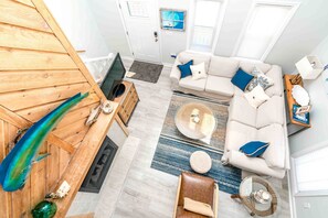 A modern living room with a wooden accent wall, a white sofa, a glass coffee table, and a wooden dining table.