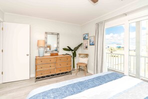 A bedroom with a bed, a dresser, a chair, a mirror, and a balcony with a view.