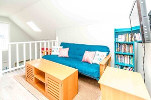 Un salon chaleureux avec un canapé bleu, des tables d’appoint en bois et une bibliothèque remplie de livres.