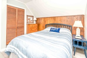 Une chambre à coucher comprenant un lit, une tête de lit en bois, une table de chevet avec une lampe, une commode et une armoire en bois.