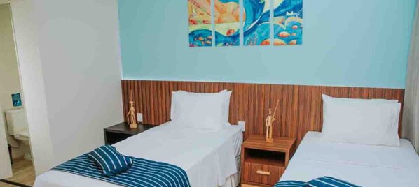 A hotel room with two beds, a wooden headboard, a nightstand with a lamp, and a wall with a colorful painting.